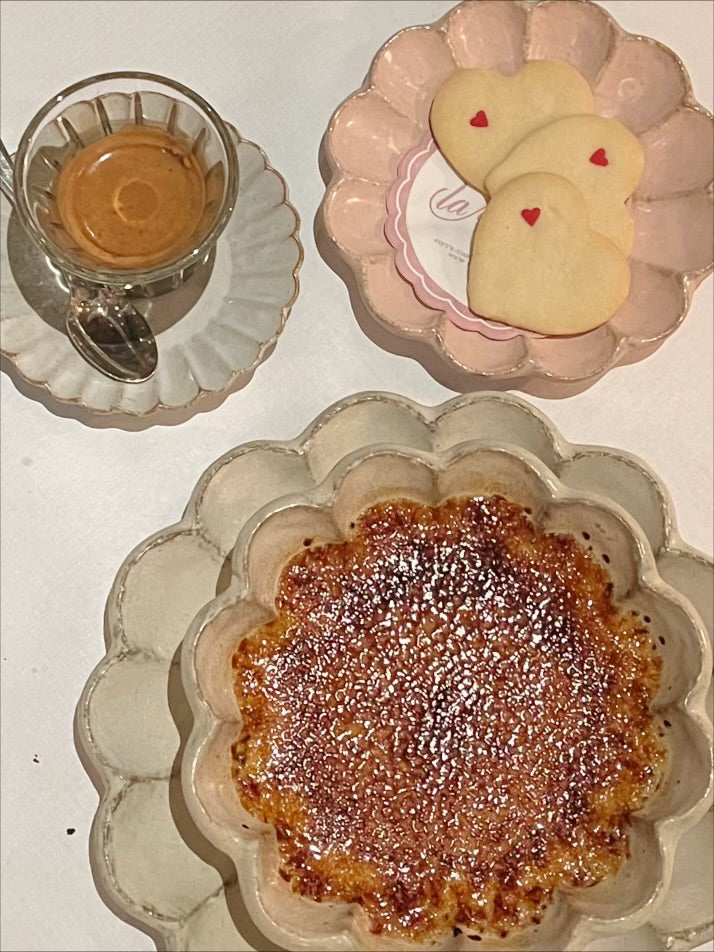 Overhead view of a café table with an amber drink, heart-shaped cookies, and a caramelized dessert