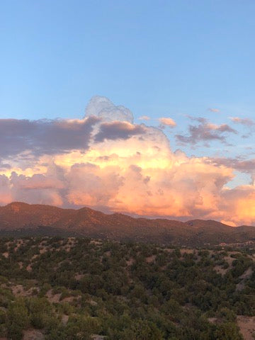 Sunset-lit clouds glowing pink and orange above scrub-covered hills and desert vegetation near Santa Fe