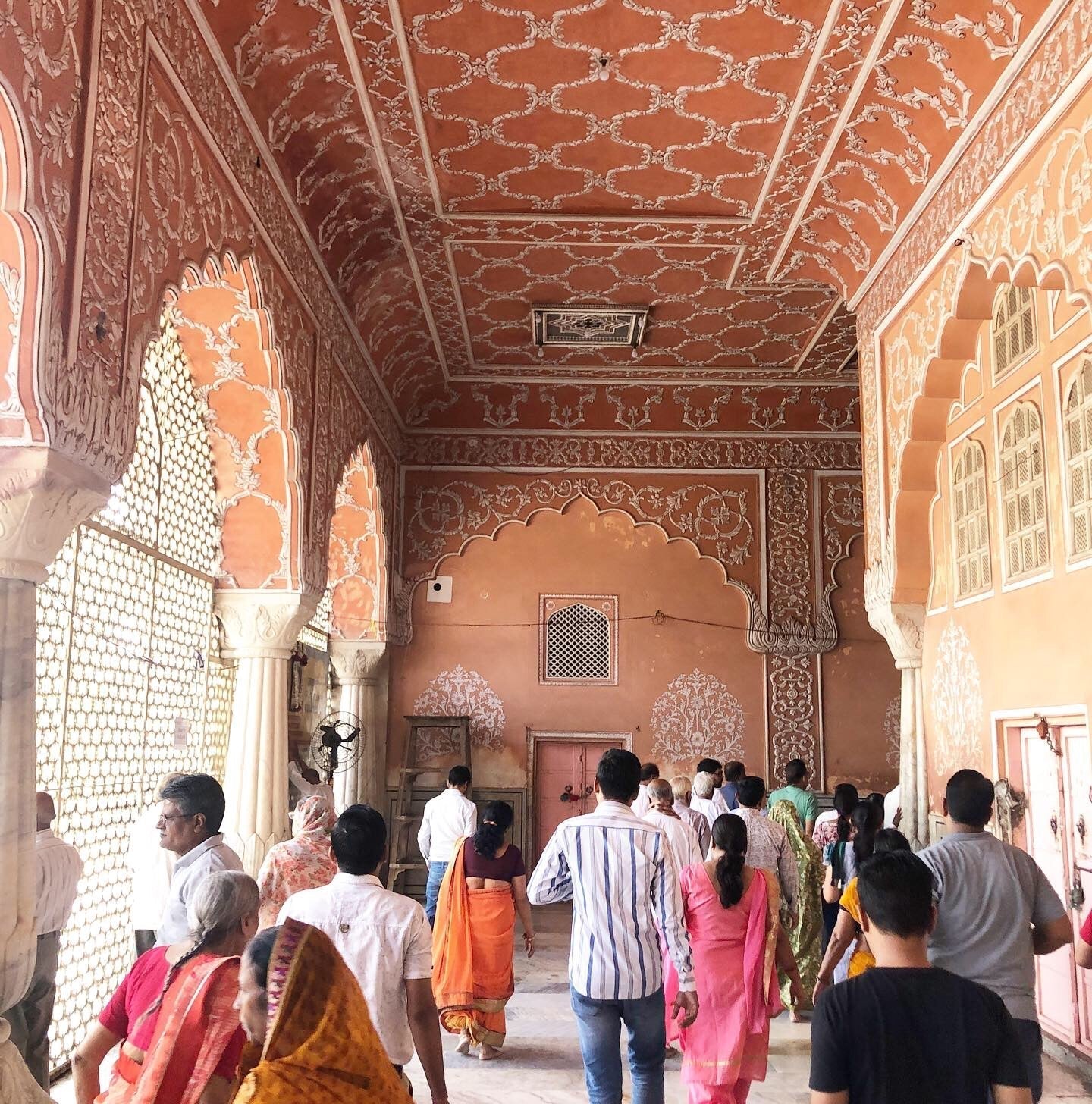 Visitors walking through a pink arched corridor with ornate white floral carvings at a historic palace in Jaipur