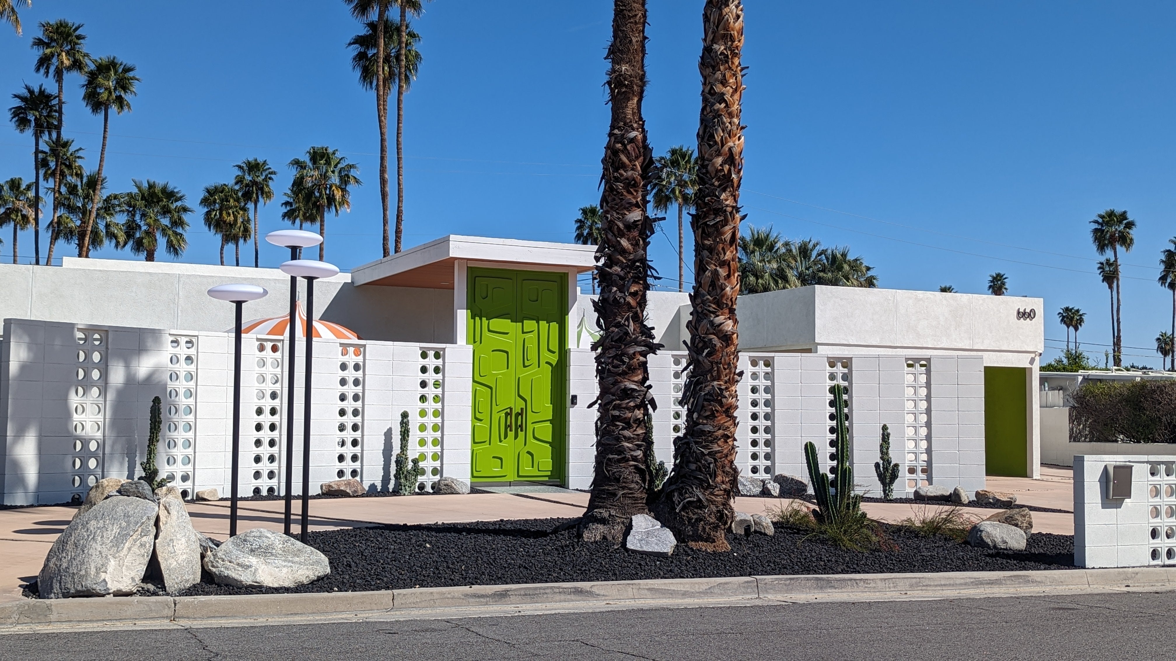 Palm Springs midcentury home with a bright green door, decorative breeze-block walls, and tall palm trees