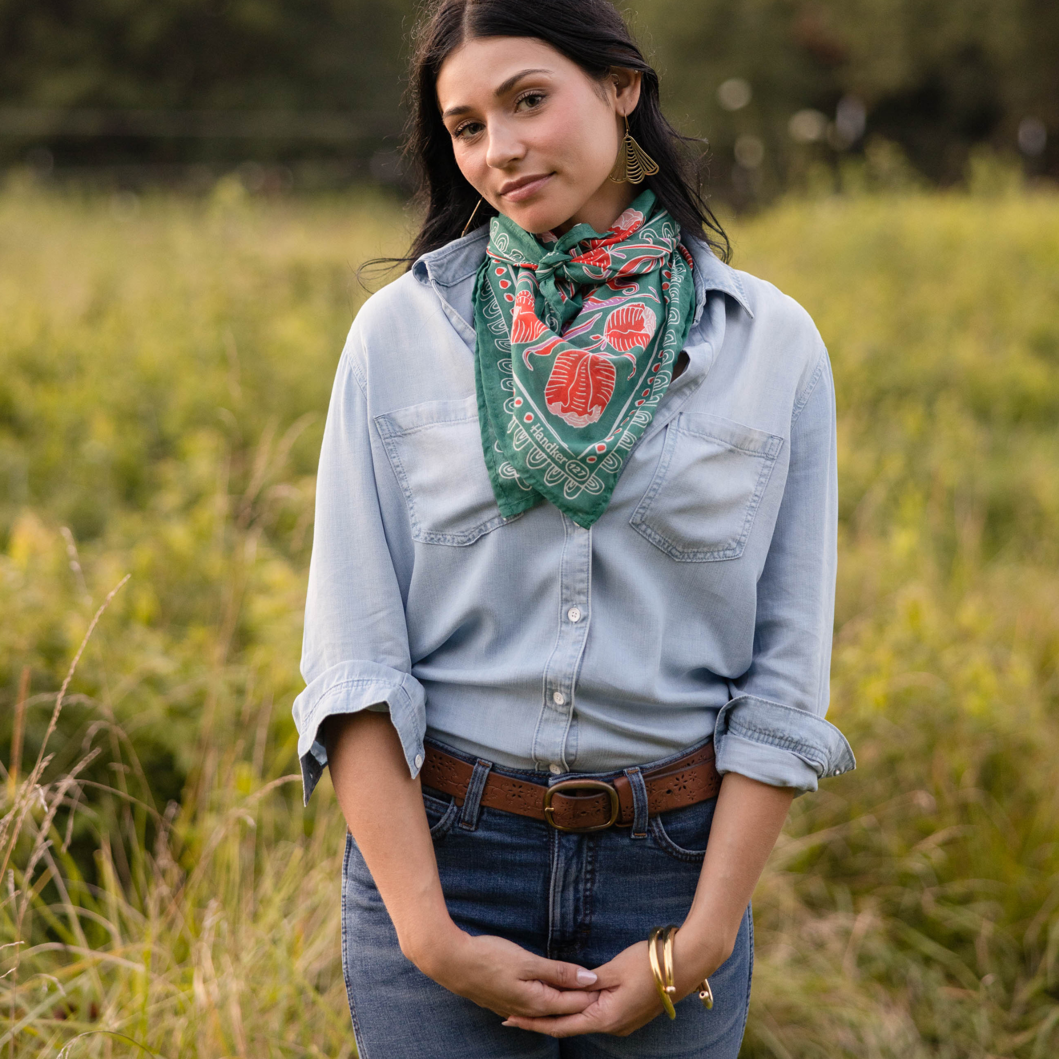 Woman wearing green floral Winnie Wild Rag bandana tied at the neck over a light denim shirt in a grassy field