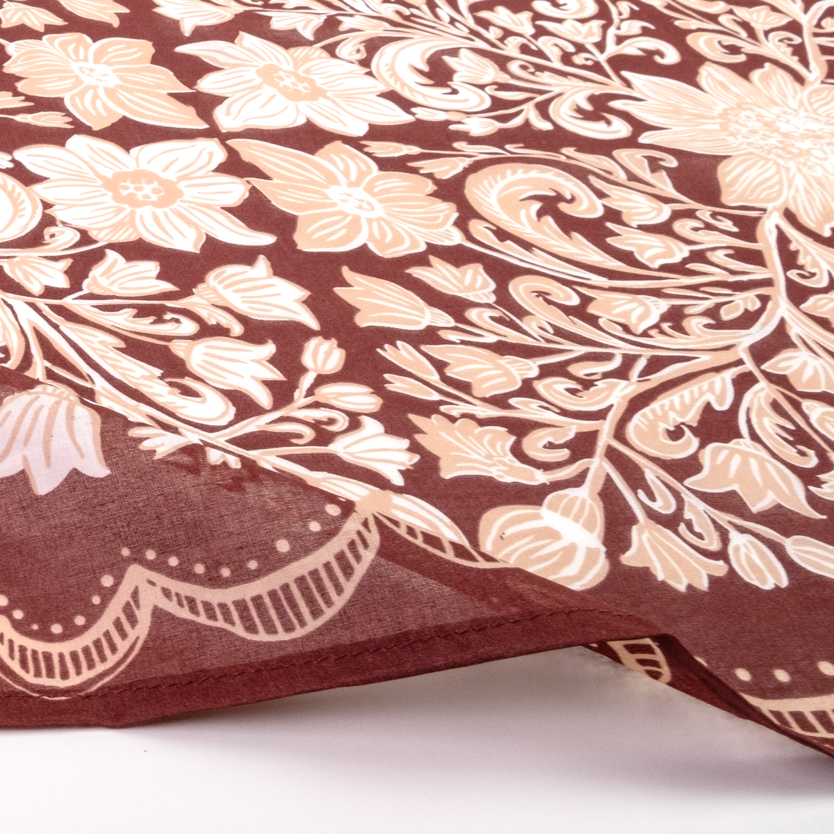 A close-up of a sheer fabric bandana with a floral and scroll pattern in cream and beige on a dark brown background.