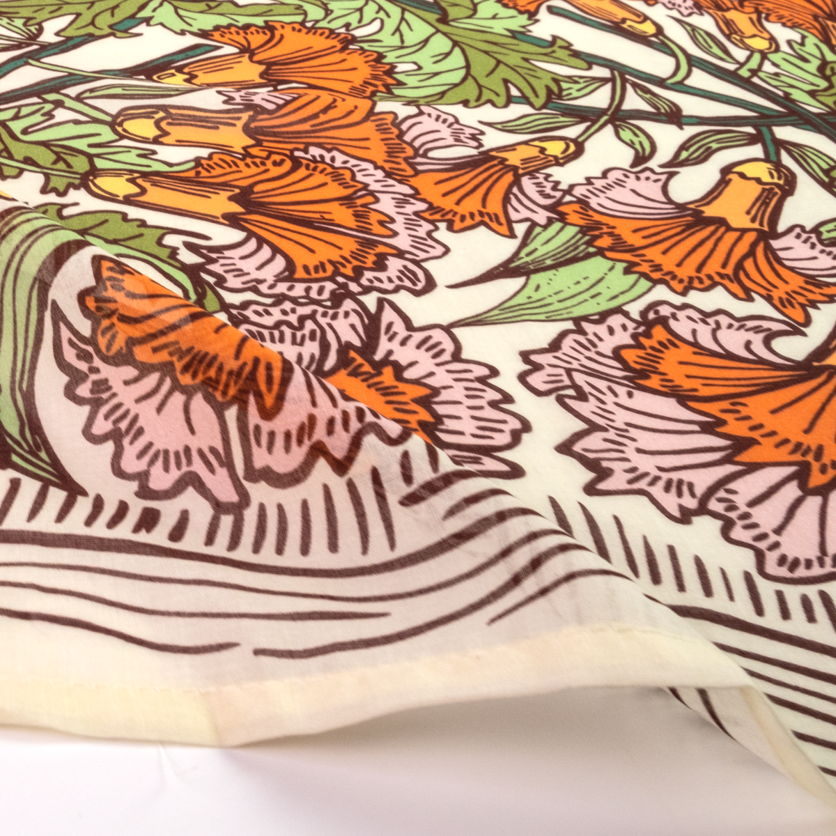 A close-up of a printed cotton bandana or scarf with a botanical pattern featuring orange flowers, pink and green leaves, and brown linework on an off-white background.