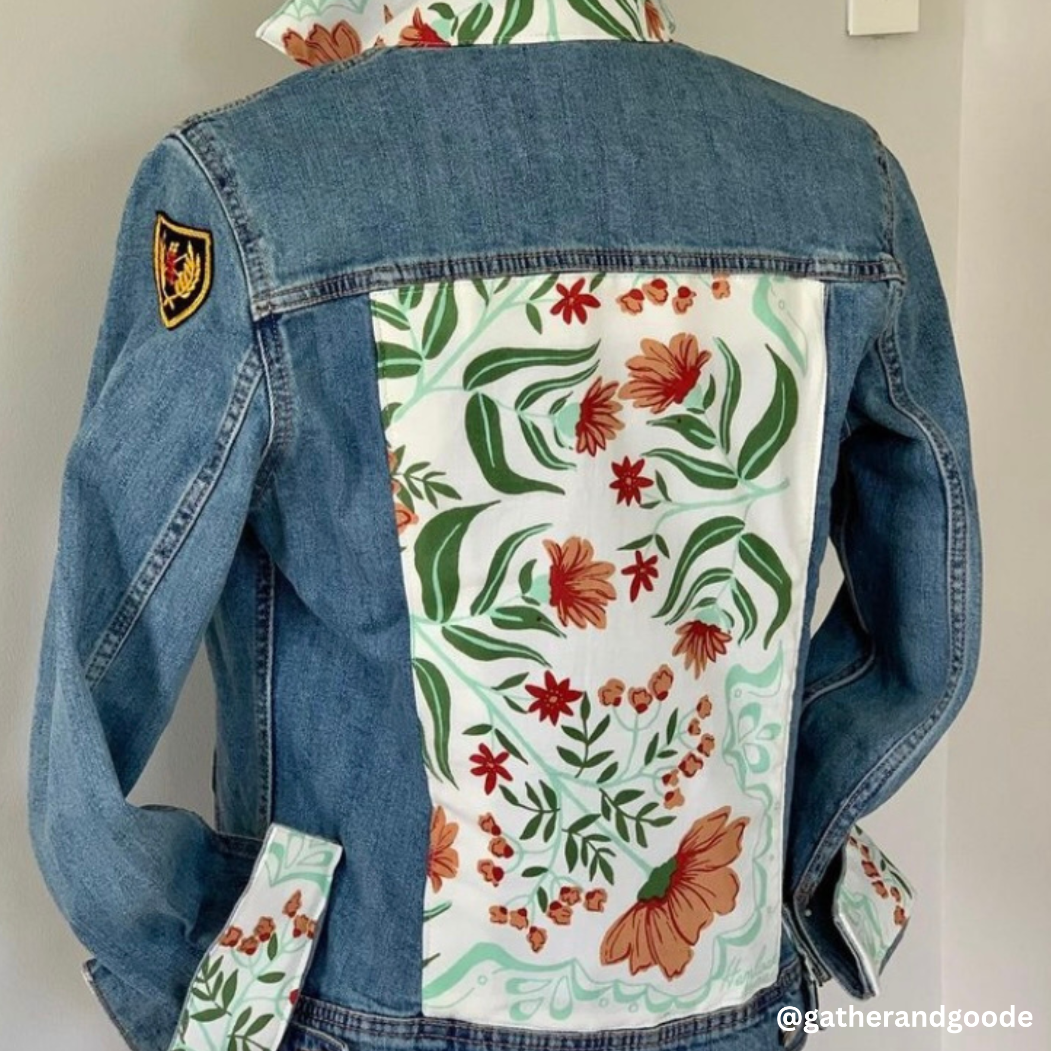 Back of denim jacket with white bandana panel showing green leaves and orange flowers and matching cuff accents on light gray background