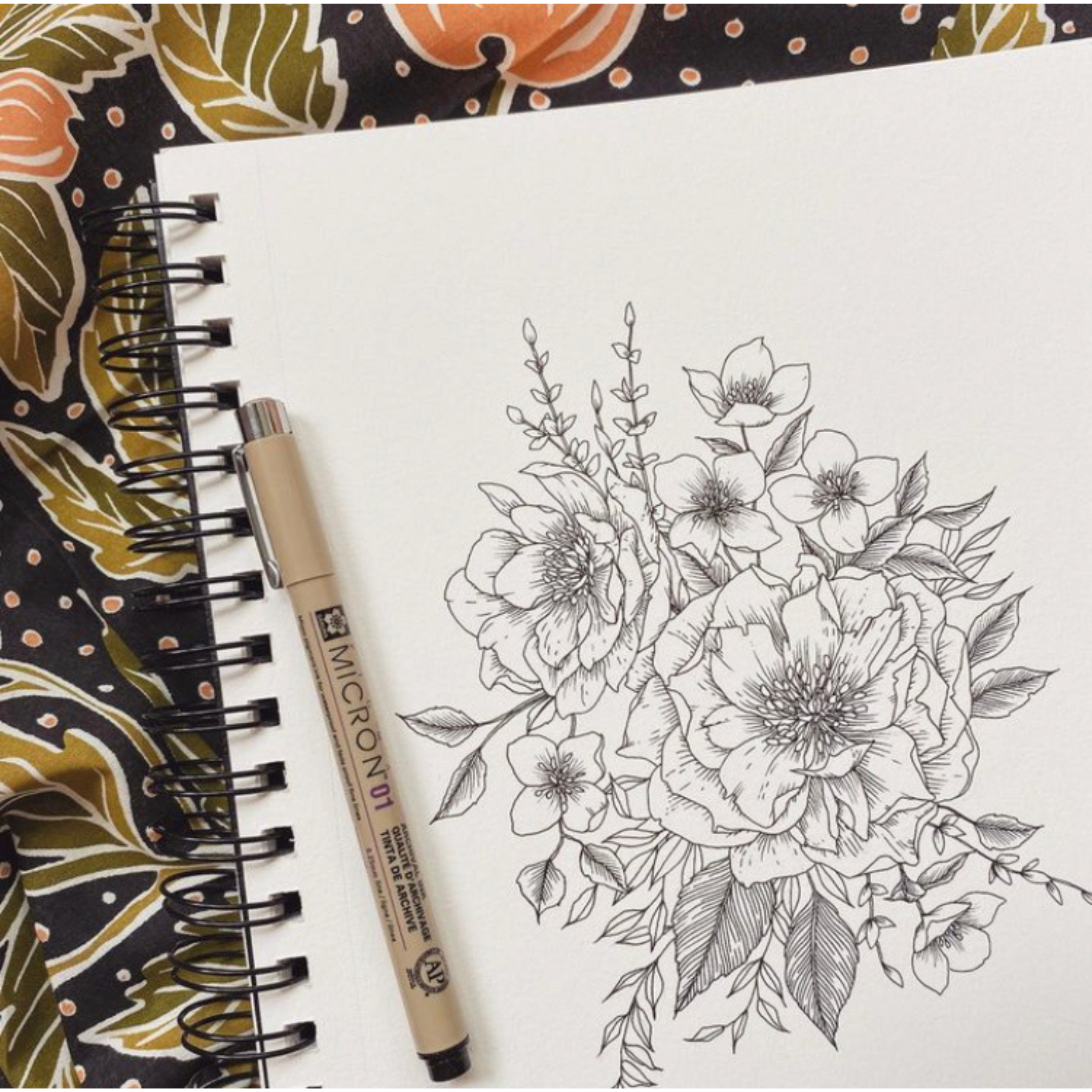 Sketchbook showing a detailed black ink floral drawing with a Micron 01 pen on a patterned bandana background