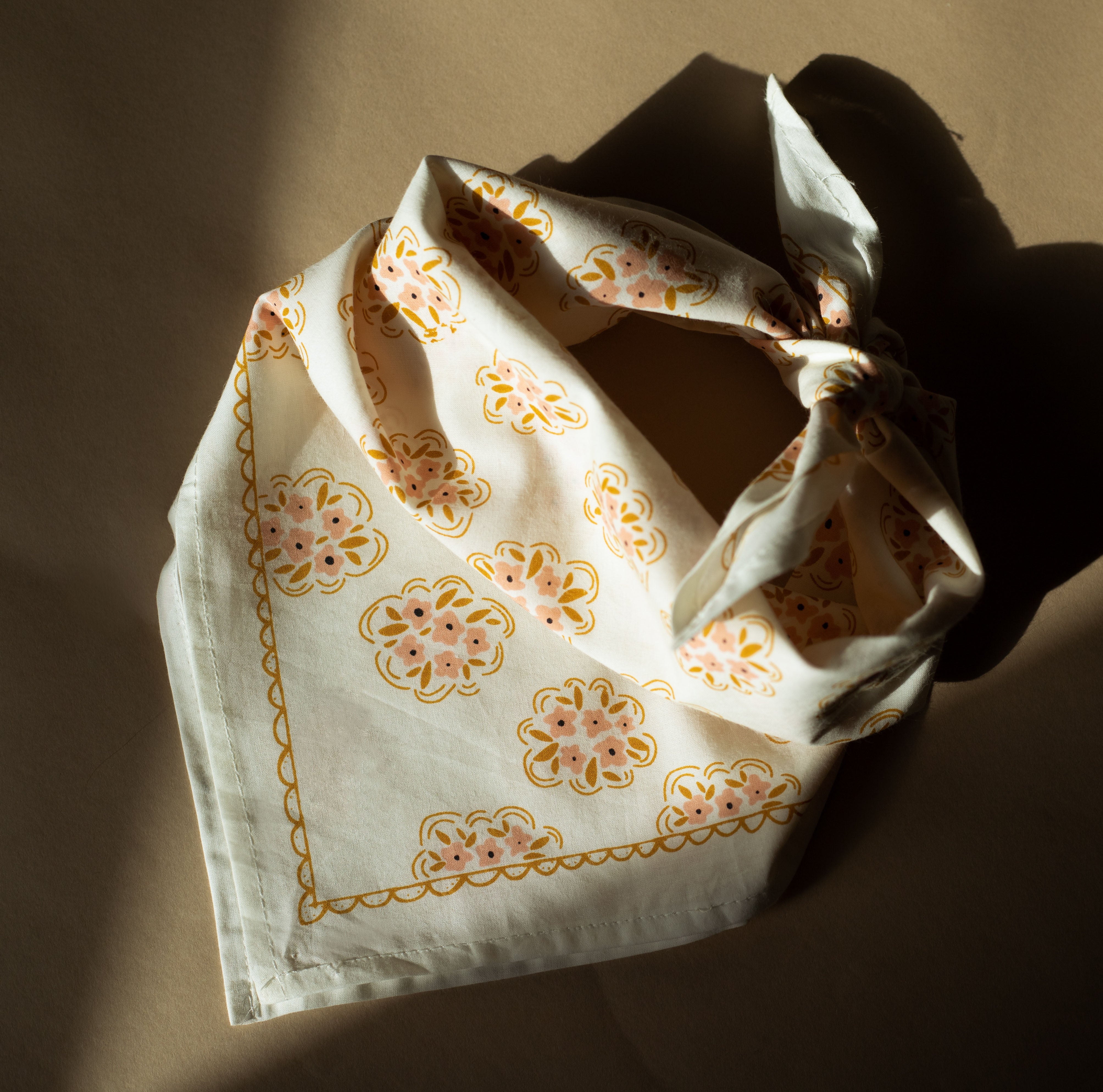 Flat-lay of No. 042 Pearl bandana showing cream with pink and gold floral medallion print and knotted corner