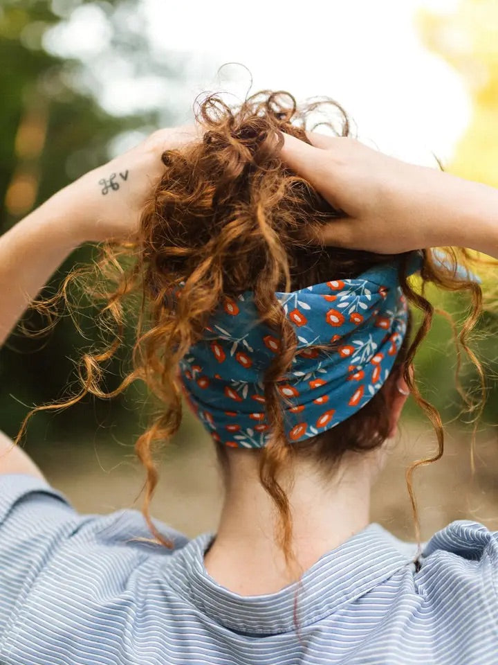 Rear view of No. 075 Juliet bandana worn as a headband showing blue fabric with red floral print on an outdoor background