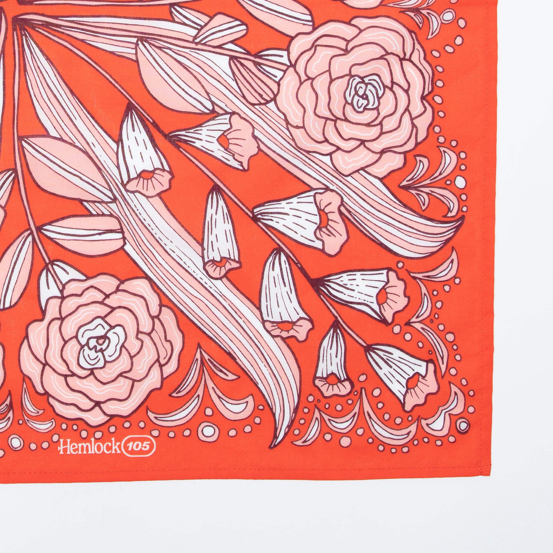 Close-up of No. 105 Greta bandana showing white and pink-peach floral print on hot-red background with Hemlock 105 corner logo
