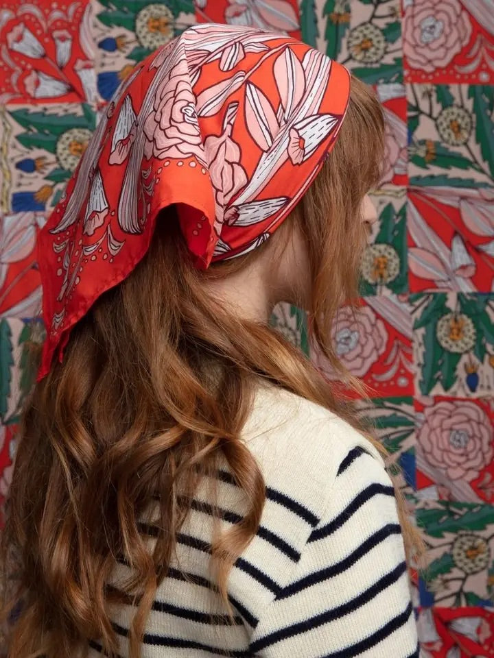 Model wearing No. 105 Greta bandana as headscarf, hot-red with white and peach floral print, side view against floral backdrop