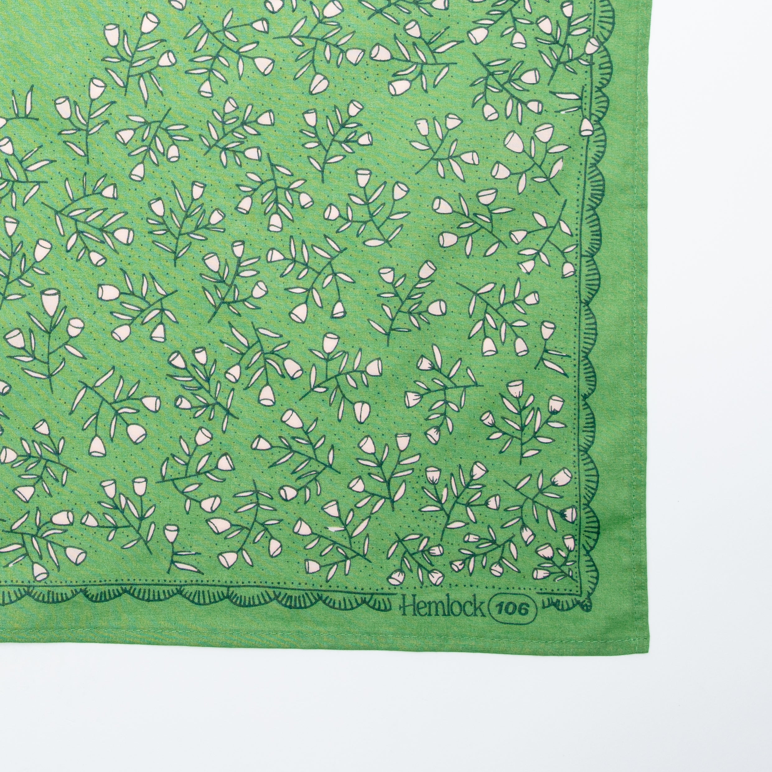 Bottom-right of Kelly Green Posey bandana with pink floral print, scalloped border and Hemlock 106 corner on white background