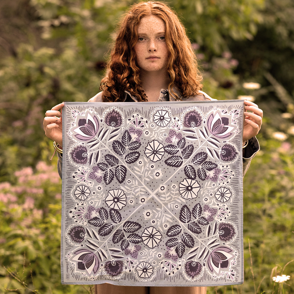 Front view of No. 113 Esther bandana held by model outdoors showcasing floral print in soft gray, cream and muted purple