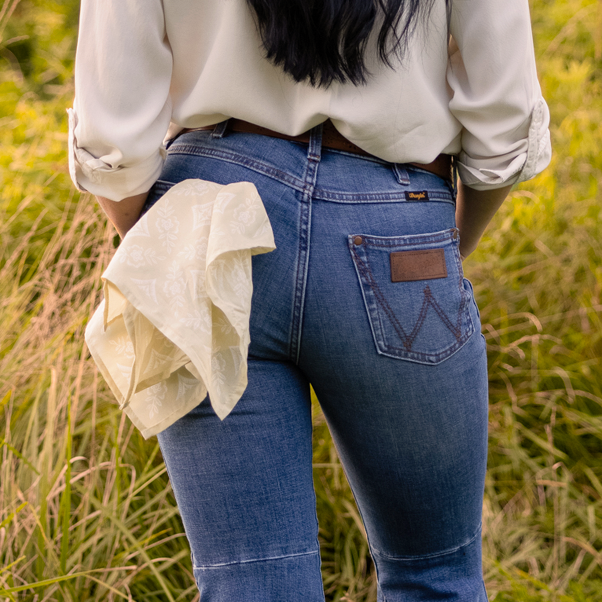 Person in jeans with a fabric hanging from the pocket, standing in a grassy field