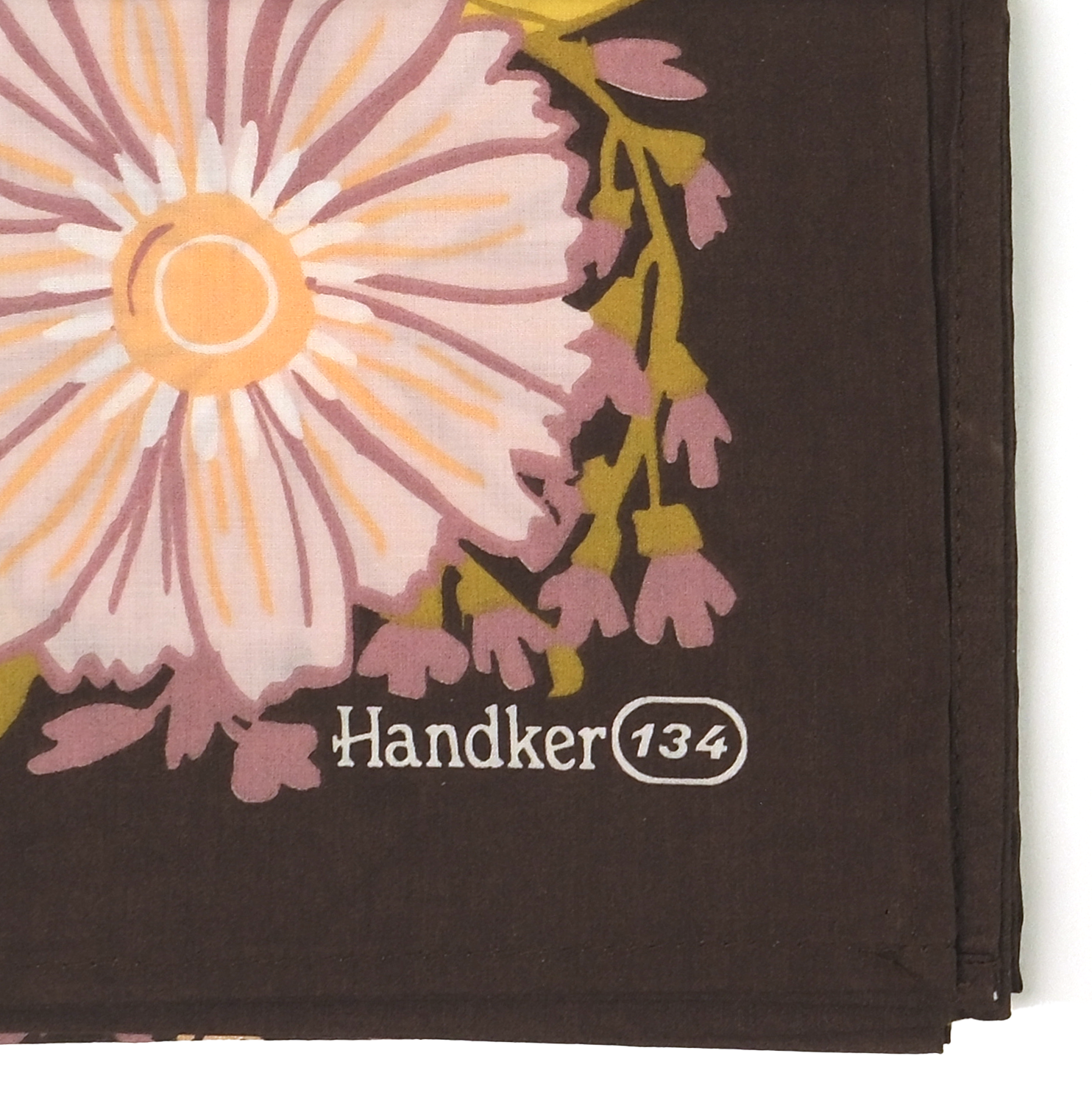 Folded corner of No. 134 Violet bandana showing a large pale violet and peach flower with olive-green leaves on a dark brown background