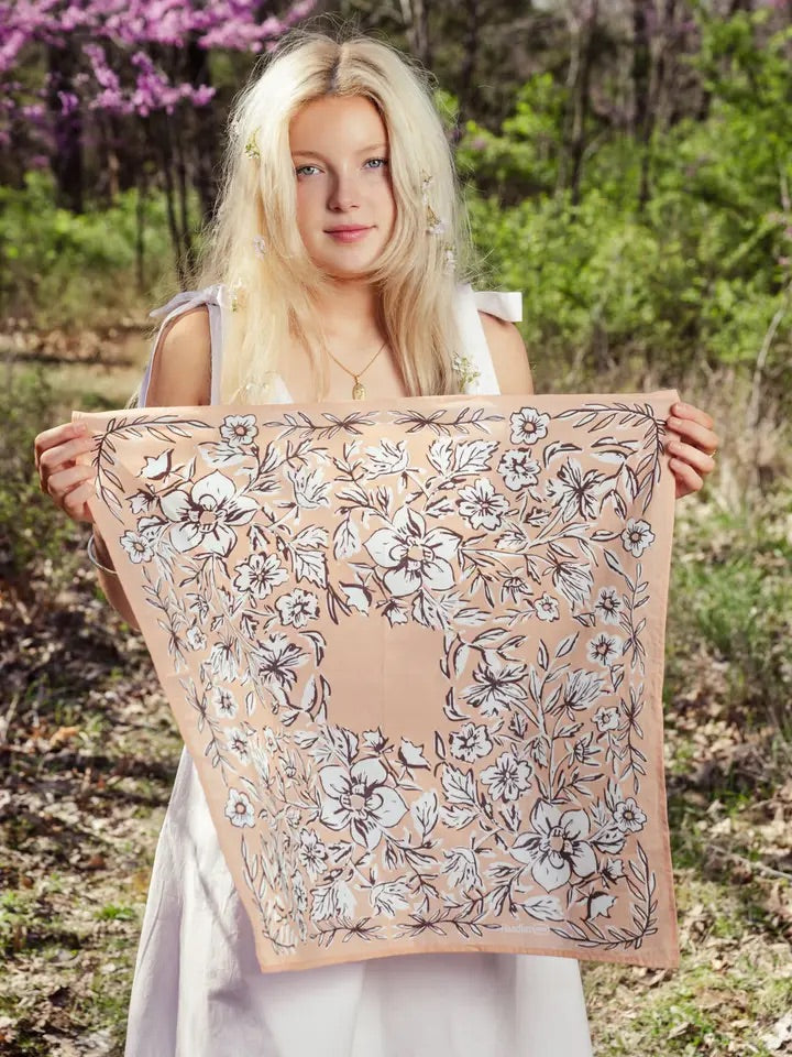 Front view of No. 135 Georgia bandana showing soft peach background with white and chocolate brown floral print held by a woman outdoors