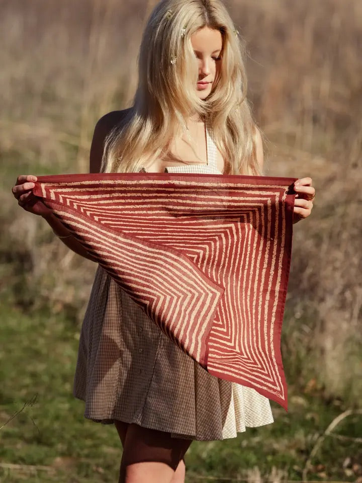 Front view of No. 136 Sammie pink stripe bandana held flat by a woman, showing concentric cream stripes in an outdoor field