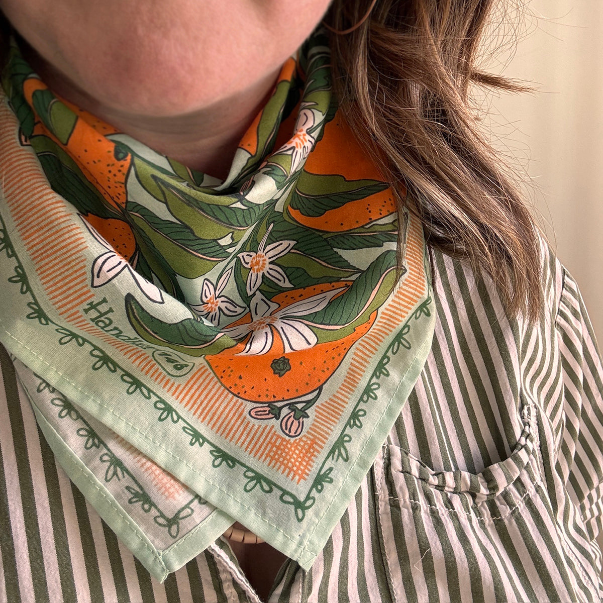 Person wearing a mint bandana with oranges, green leaves, and white flowers