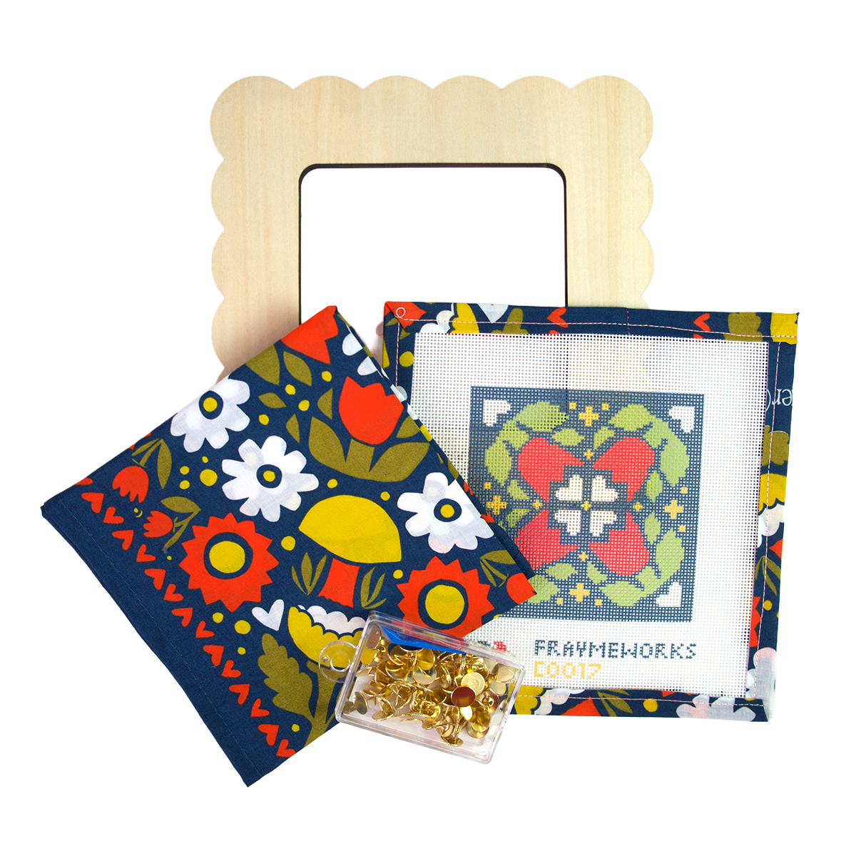 A cross-stitch bundle with a cotton bandana with an orange, green, yellow, and white floral pattern on a dark blue background, a matching floral cross-stitch piece, a wooden scalloped frame, and a small container of gold pins.