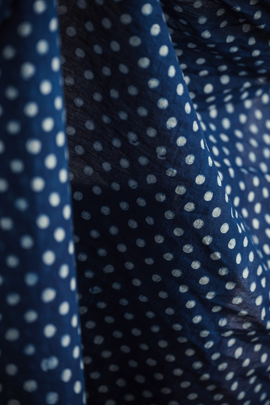 Navy blue fabric draped in soft folds with small white polka dots