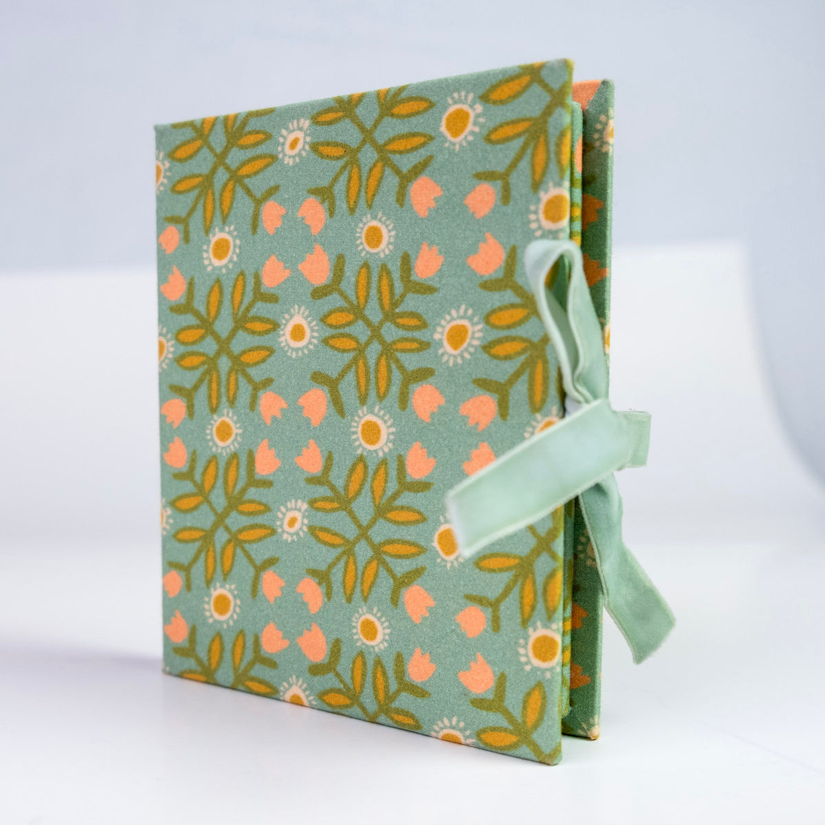 Three-quarter view of Katie Fabric Folio Frame showing green floral fabric cover and ribbon tie on white background