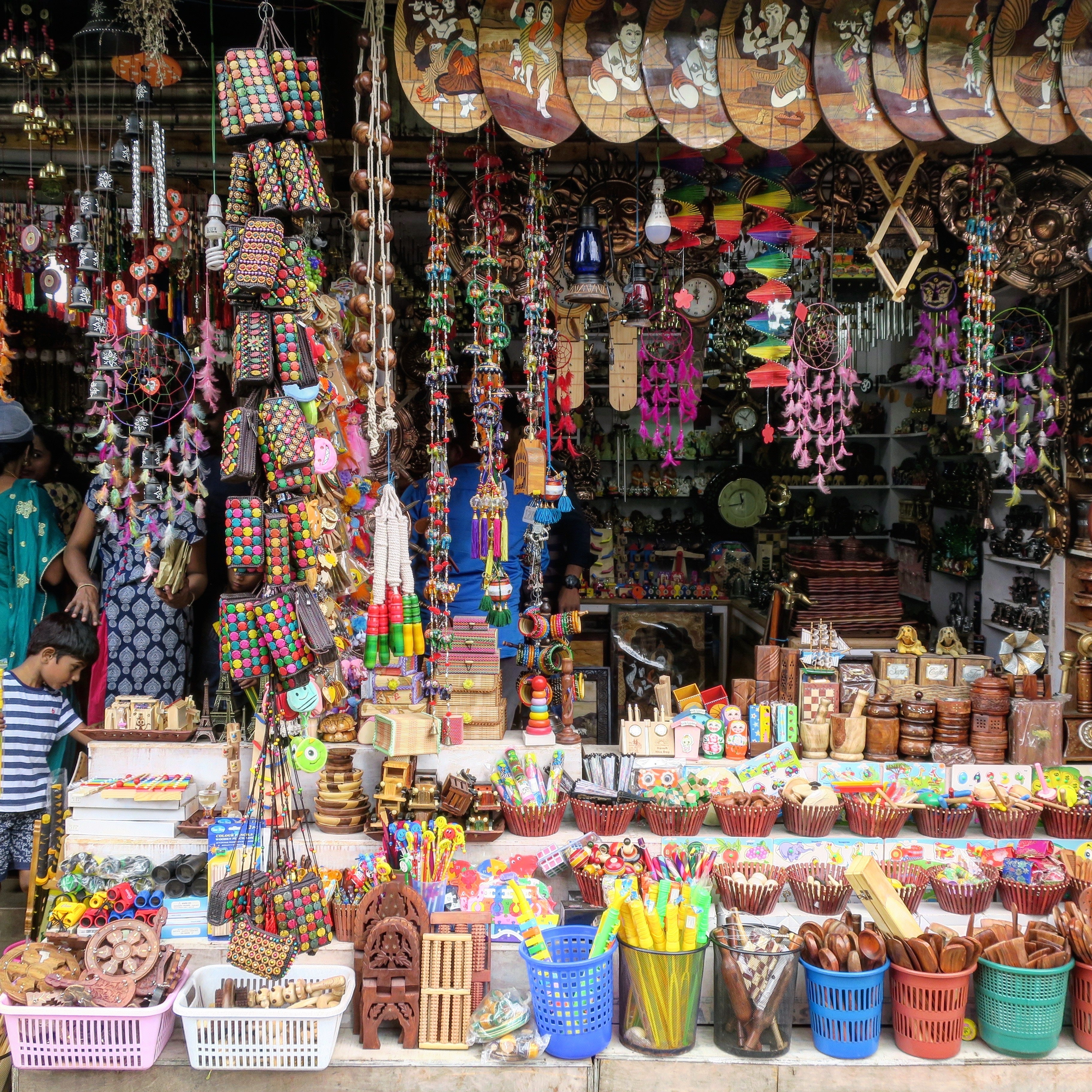 Colorful outdoor market stall packed with hanging ornaments, dreamcatchers, wooden toys, baskets, and small handcrafted trinkets