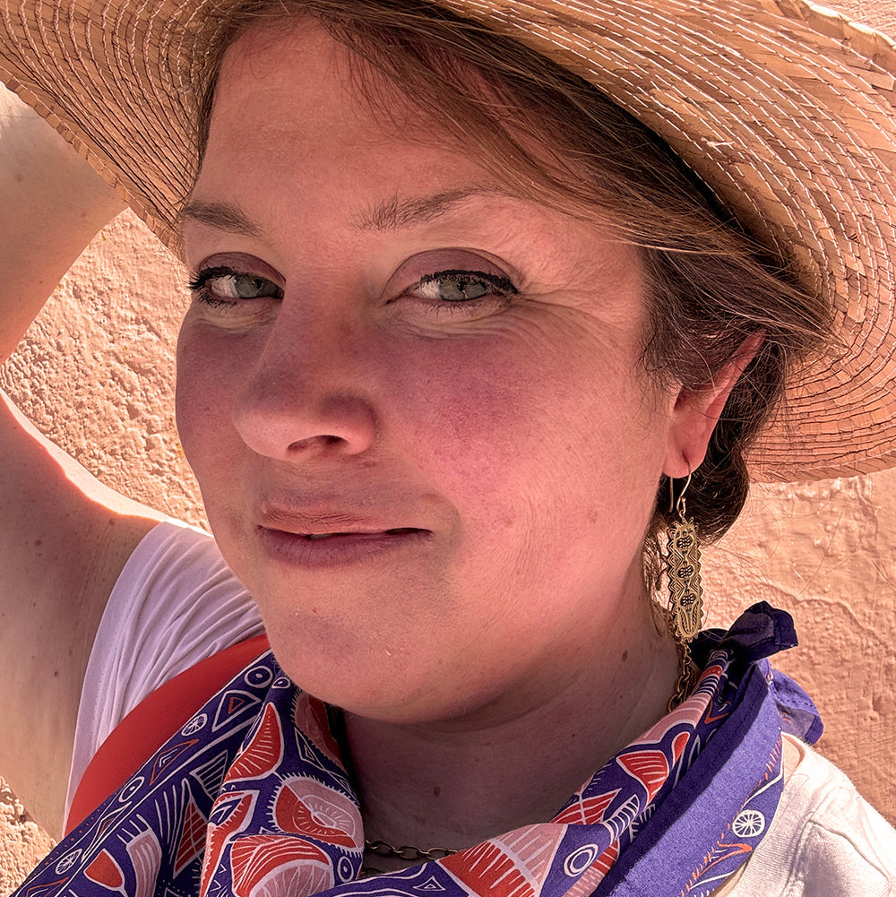 Woman wearing a straw hat and patterned scarf smiles at the camera.