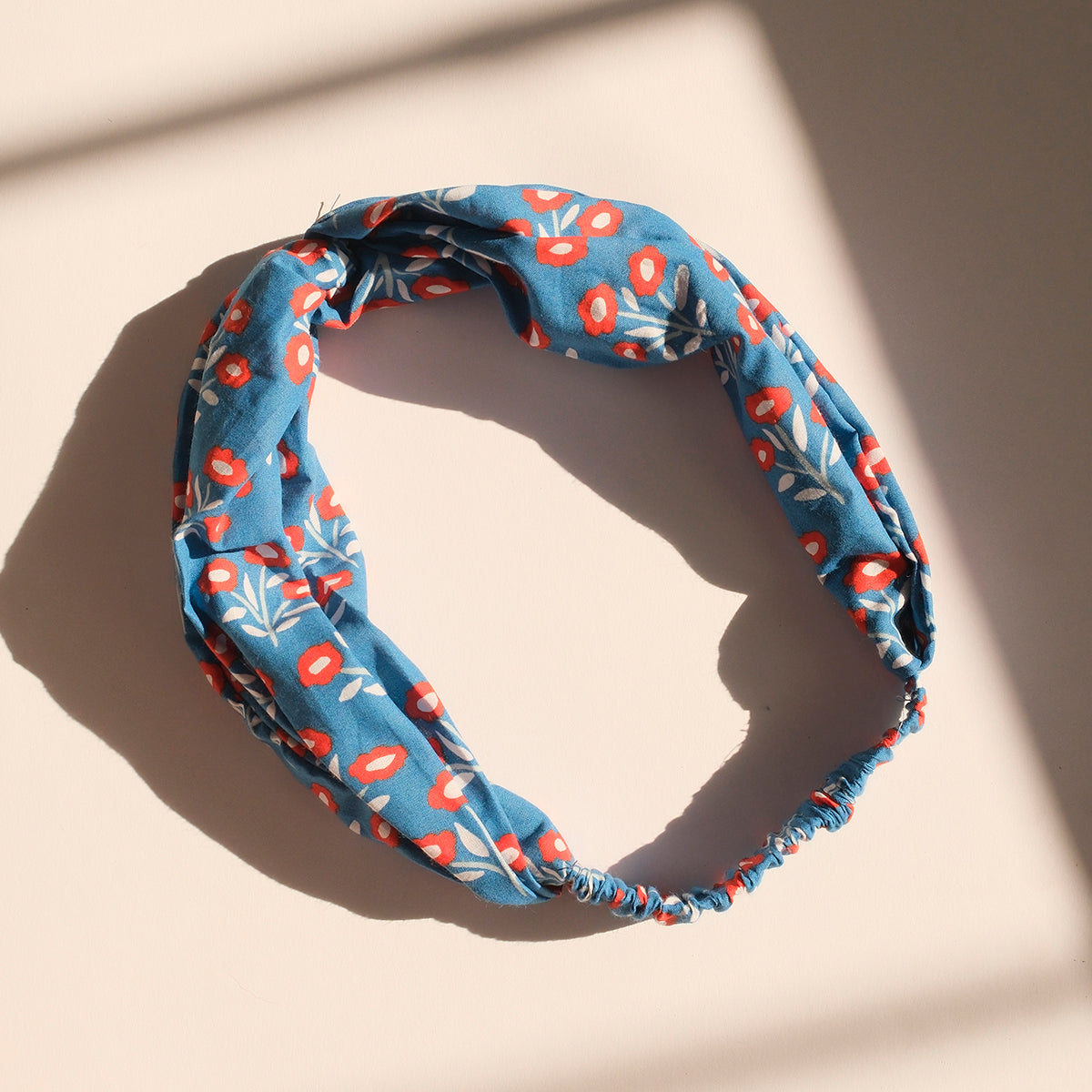 Blue knotted elastic headband with red and white floral print on light background