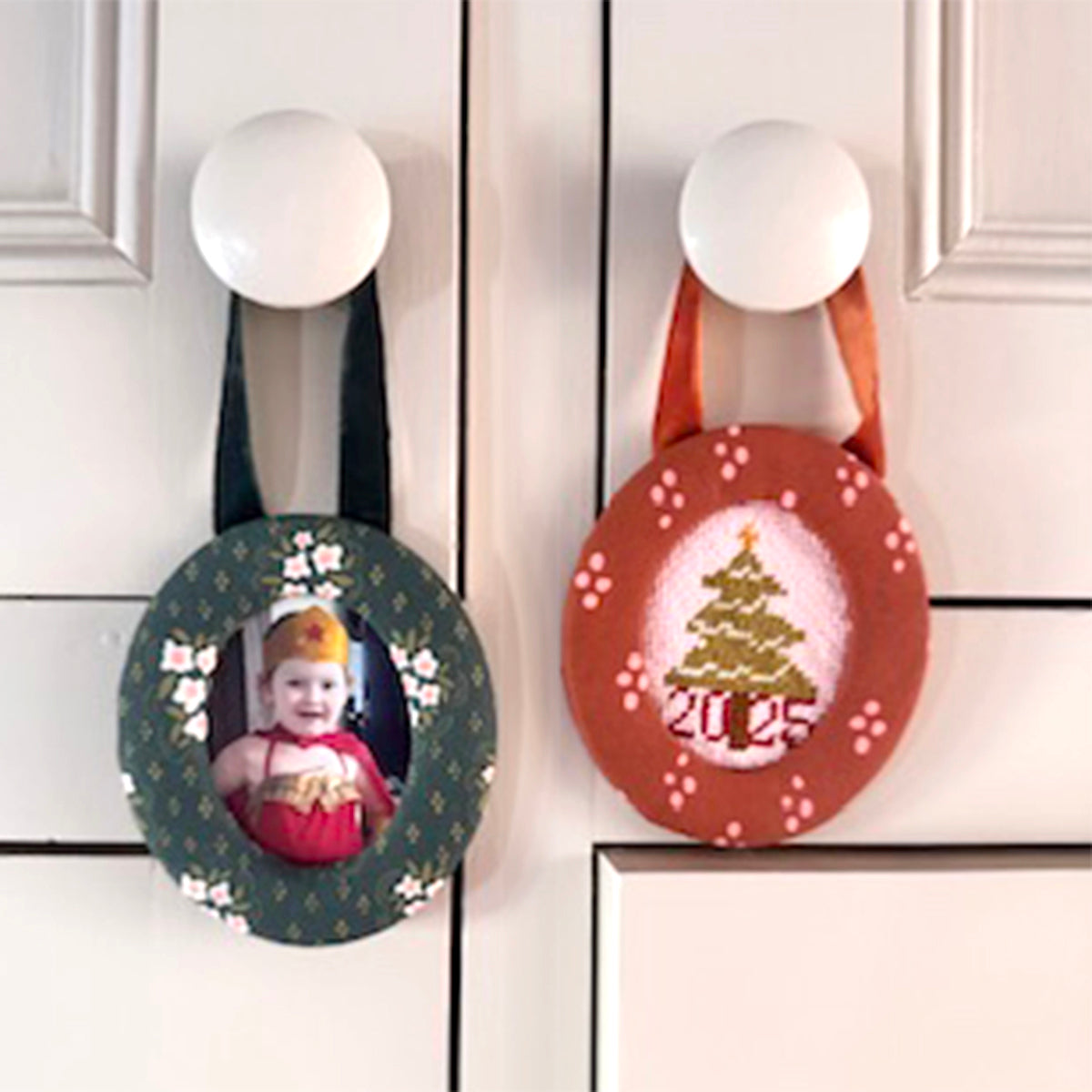 Two ceramic holiday ornaments hanging from cabinet knobs; left holds a child's photo, right shows a painted Christmas tree.