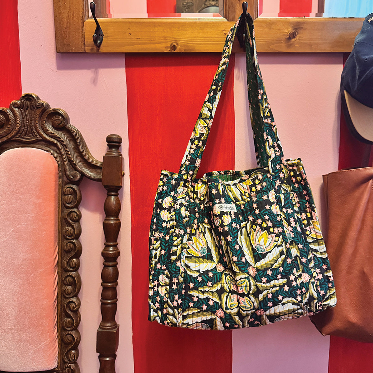 Green and yellow floral-patterned shoulder bag hanging from a wooden peg rack next to an upholstered chair