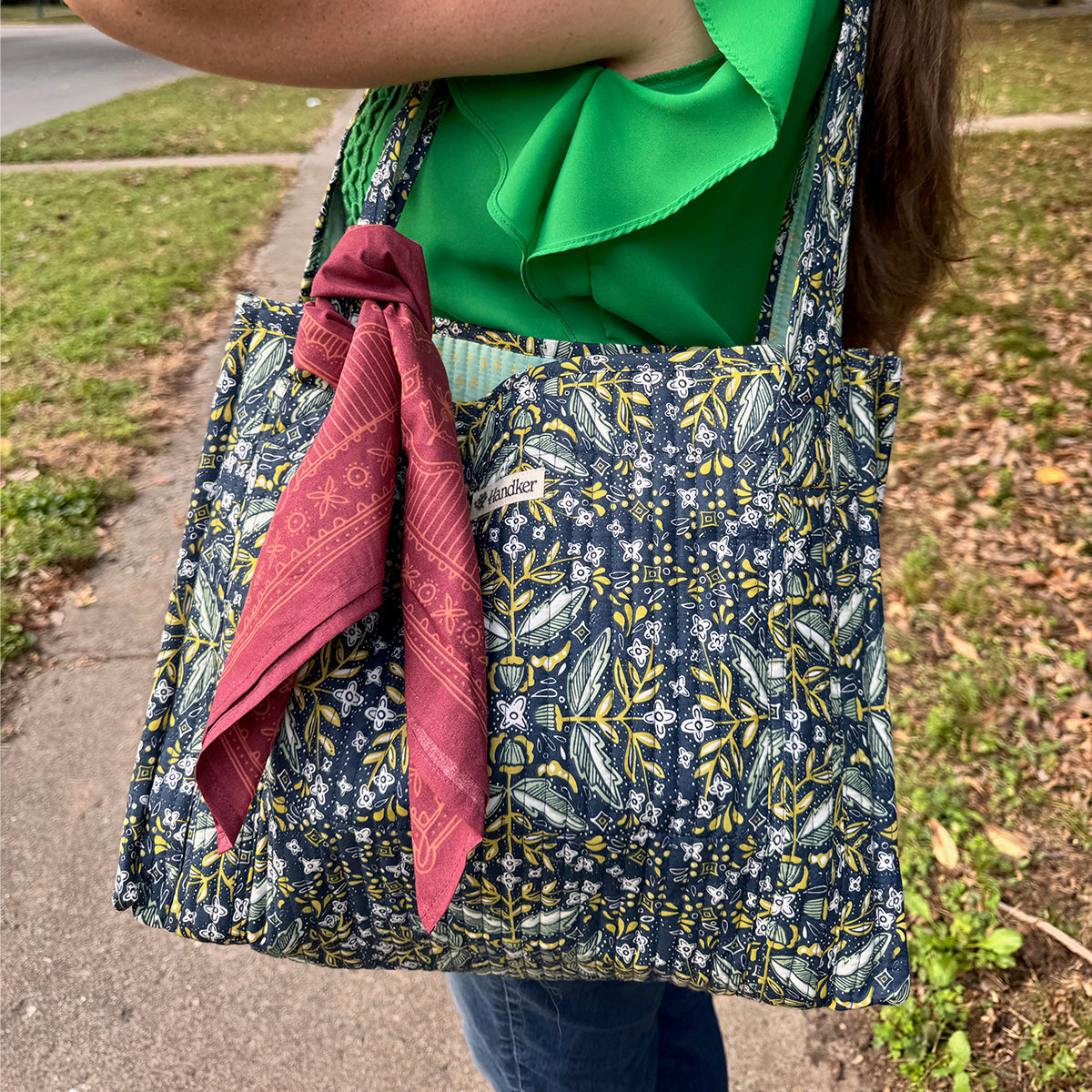 Quilted blue and yellow floral tote with braided straps and a red bandana tied to the handle, worn over shoulder