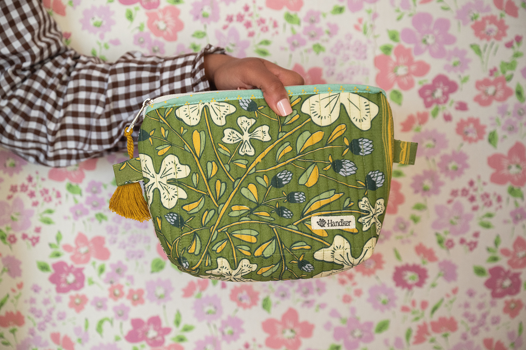 Green floral-patterned pouch held by a person on a floral background