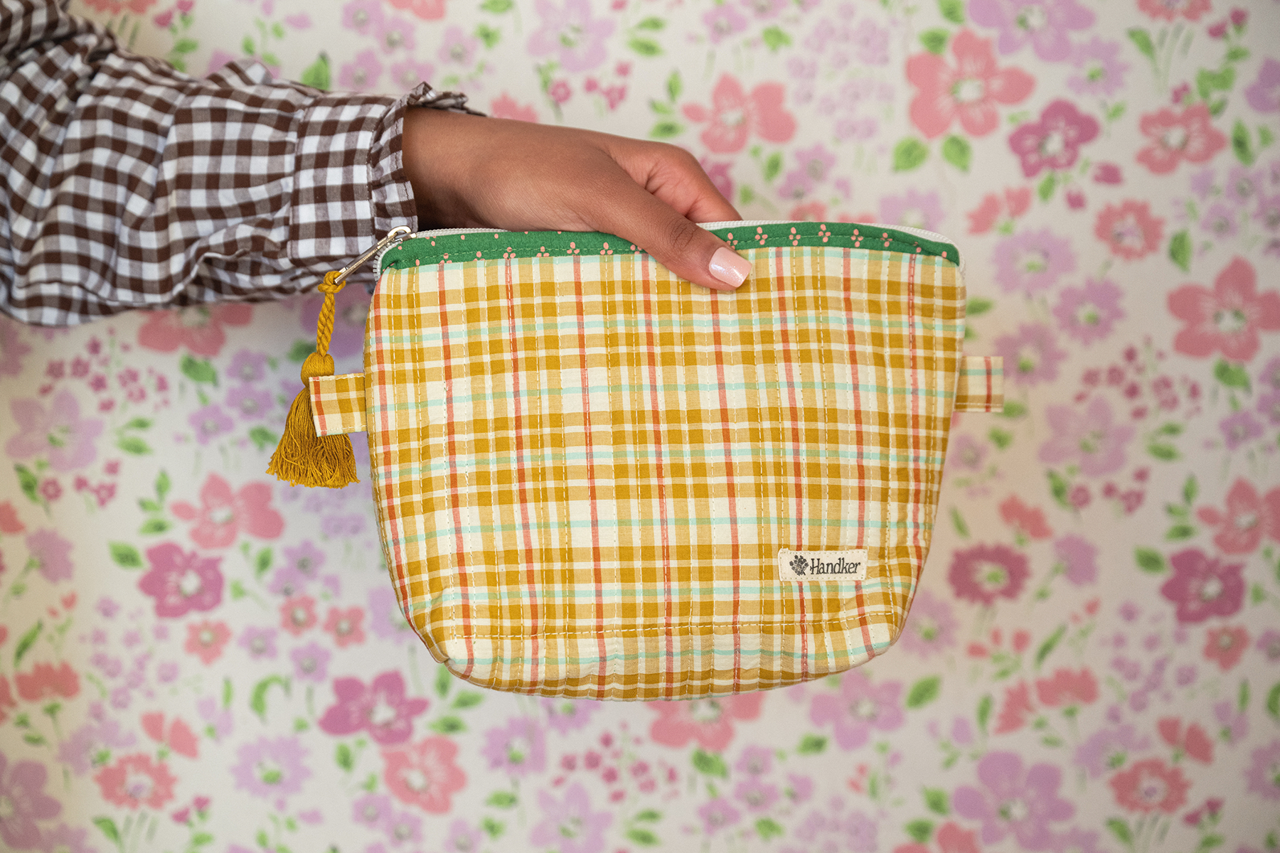 Person holding a yellow checkered pouch with a floral background