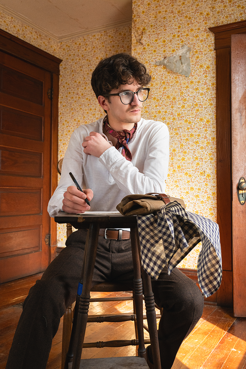 Stool view of No. 149 Teddy Bandana, navy and cream plaid, draped to show yarn-dyed plaid beside seated model in floral room