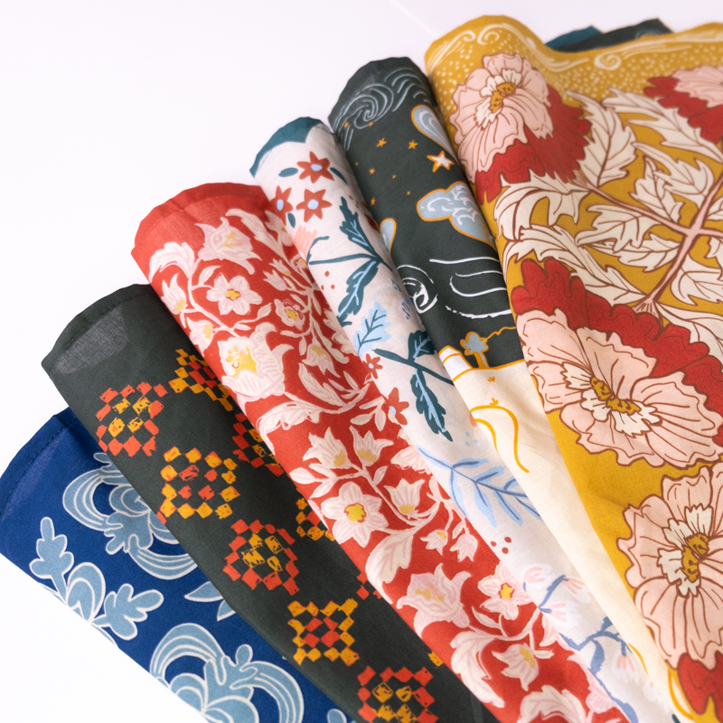 Angled view of six Series 18 22 inch bandanas fanned to show colorful travel-themed prints on white background