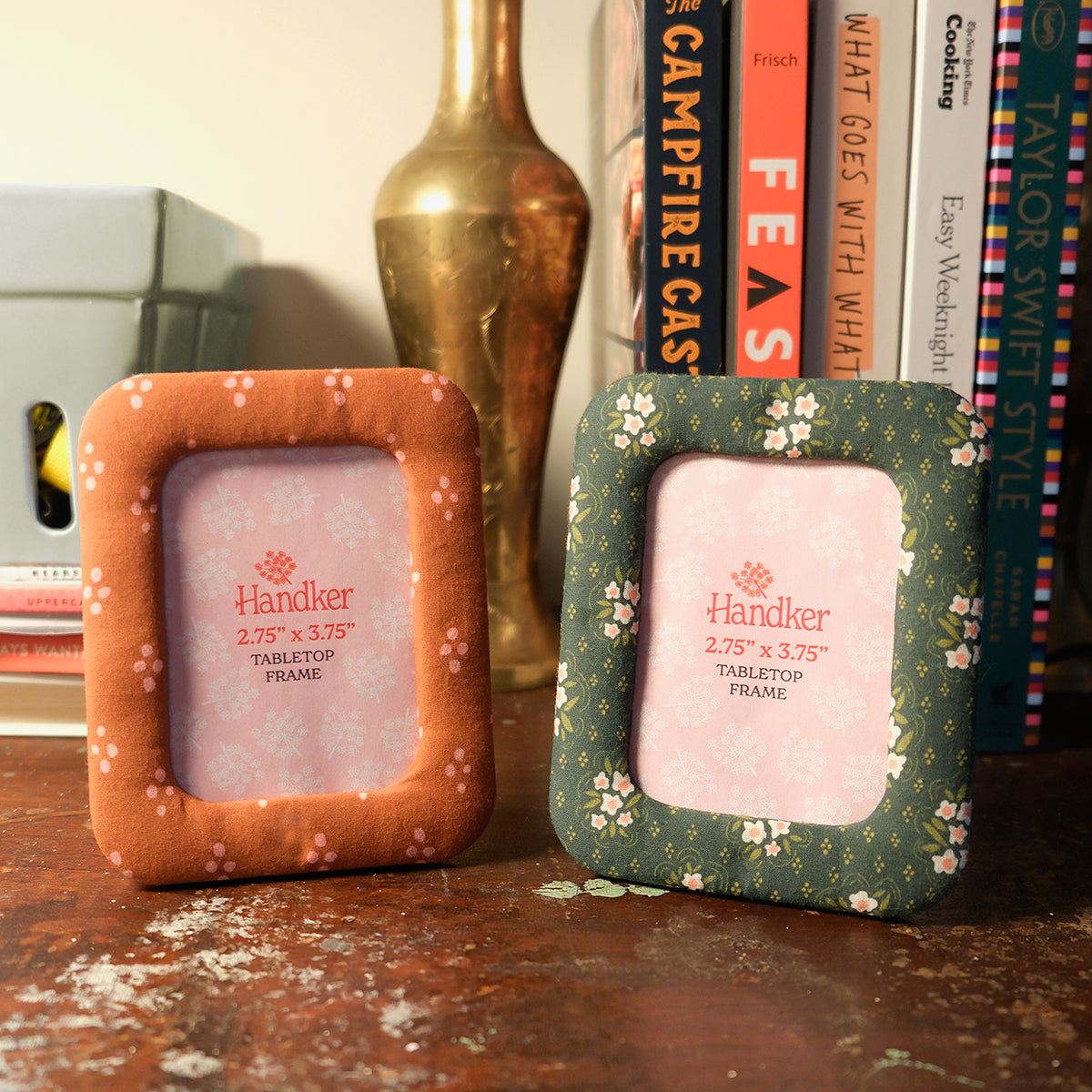 Two speckled ceramic tabletop frames, one orange and one green, holding square placeholder photos on a wooden shelf.