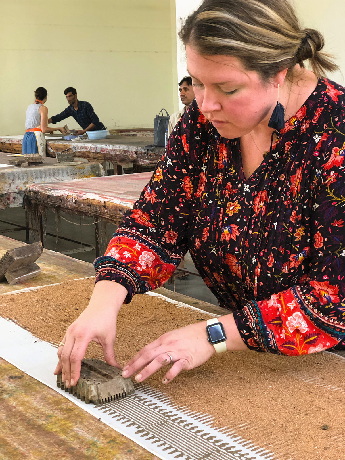 Person stamping a hand-carved wooden block to apply dabu mud-resist pattern on fabric in a Jaipur workshop