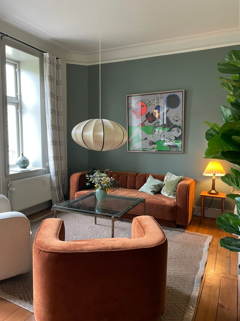 Copenhagen living room with a rust-colored sofa, sculptural pendant lamp, framed artwork, and leafy plants