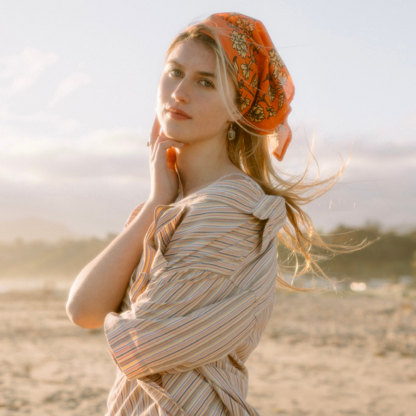 Woman with an orange scarf standing on a beach.