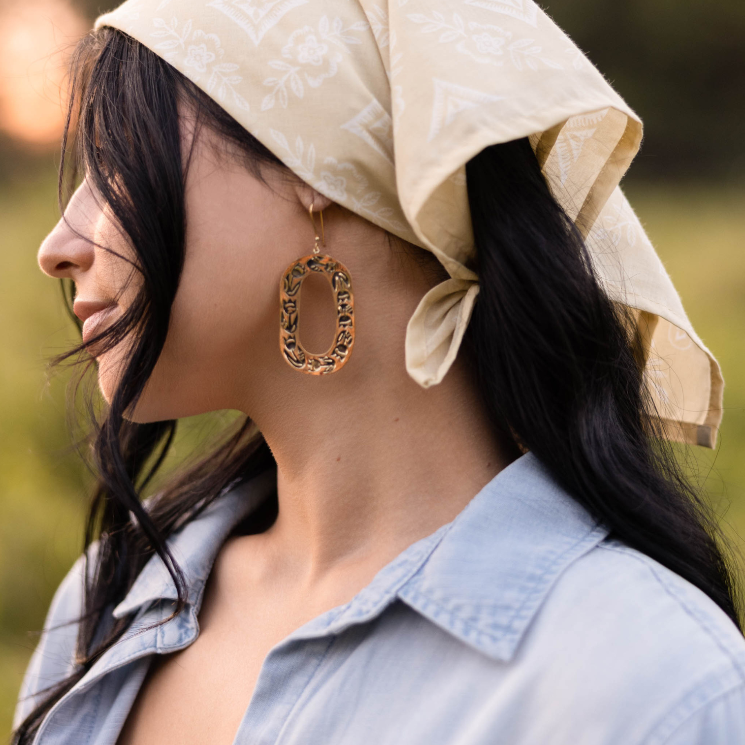 Woman with dark hair wearing a patterned headscarf and large hoop earrings.