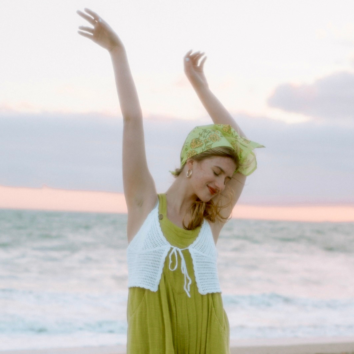 Person enjoying a serene moment at the beach with arms raised and eyes closed.