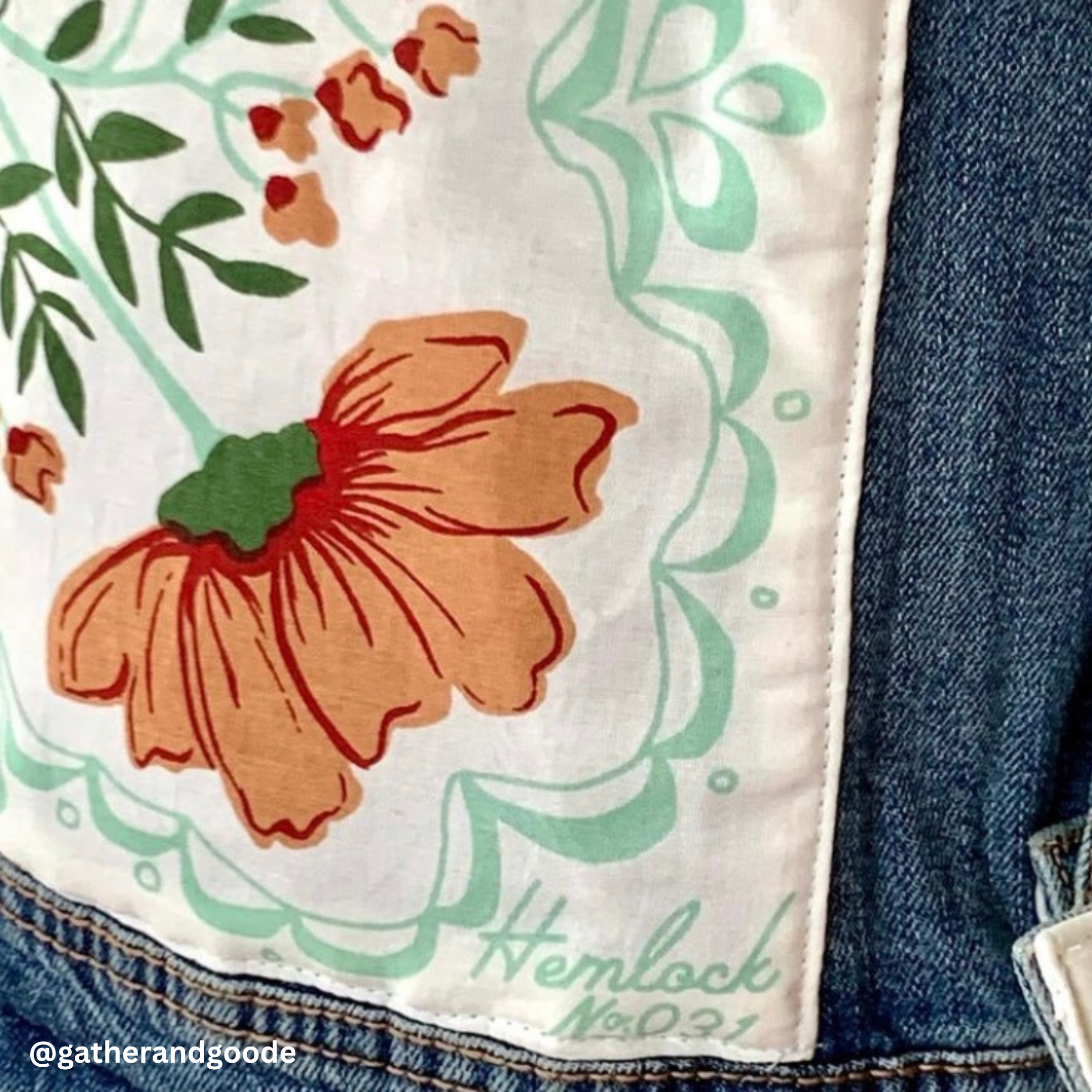 Close-up of a bandana corner showing an orange floral print and Hemlock No. 31 signature on white fabric against denim