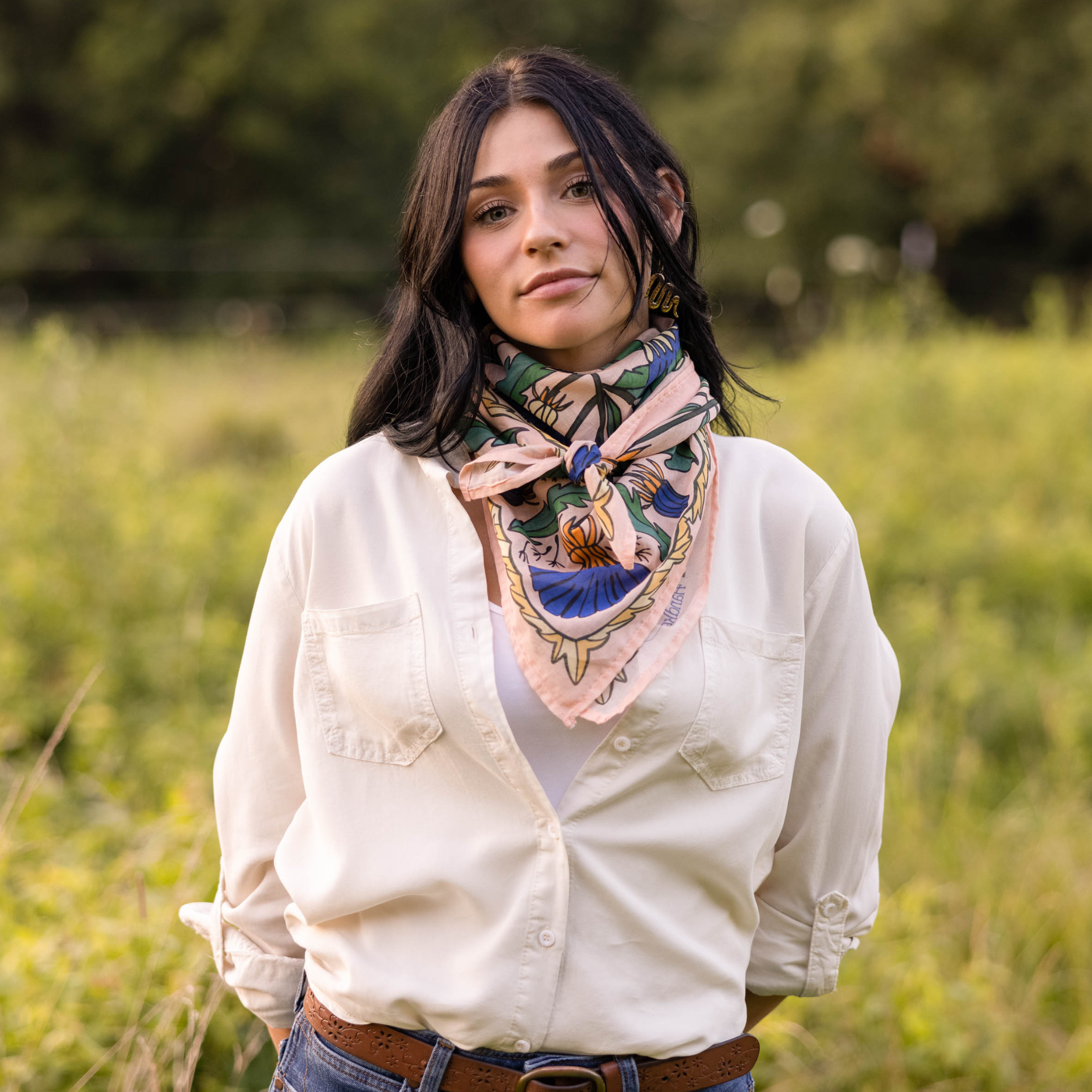 Woman in white shirt with colorful scarf standing in a grassy field
