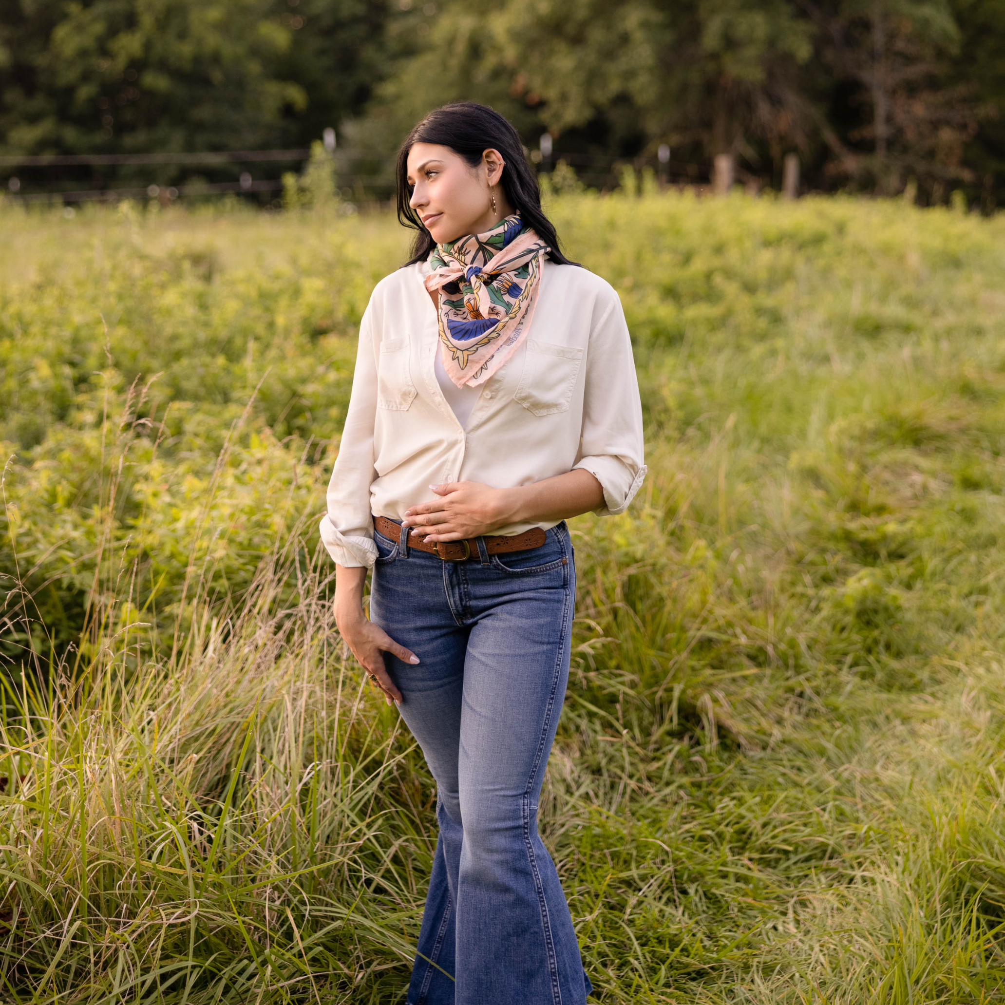 Woman standing in a grassy field wearing a white shirt and scarf