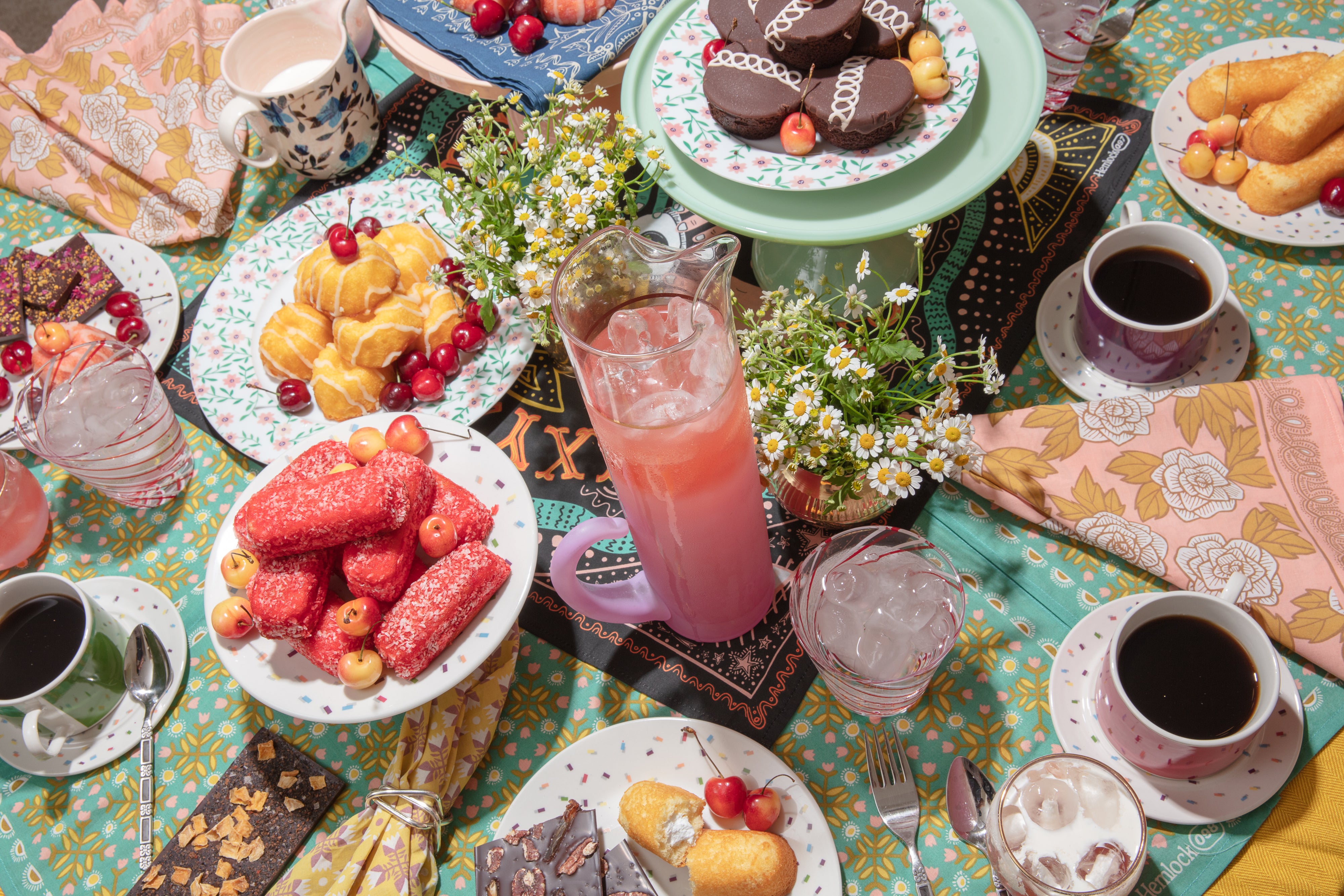 Overhead tablescape of bandana napkins and a bandana tablecloth set with assorted pastries, coffee cups, and a pitcher of pink drink