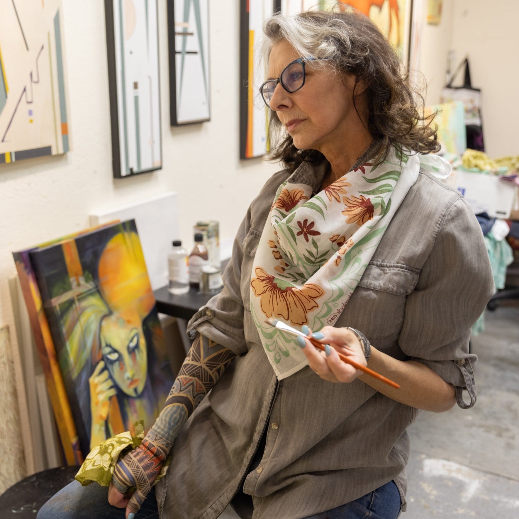 Artist in studio holding a paintbrush with paintings in the background