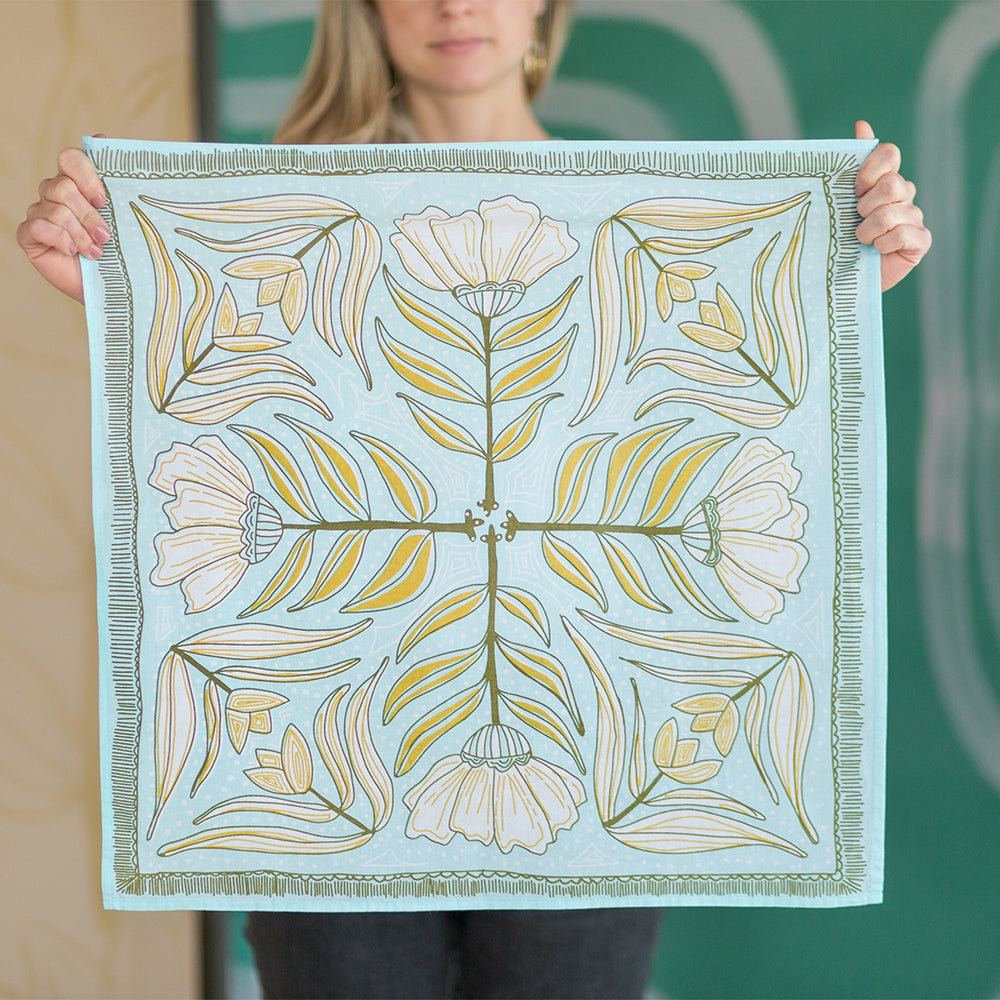 Person holding a floral patterned cloth with green and yellow design on light blue background.