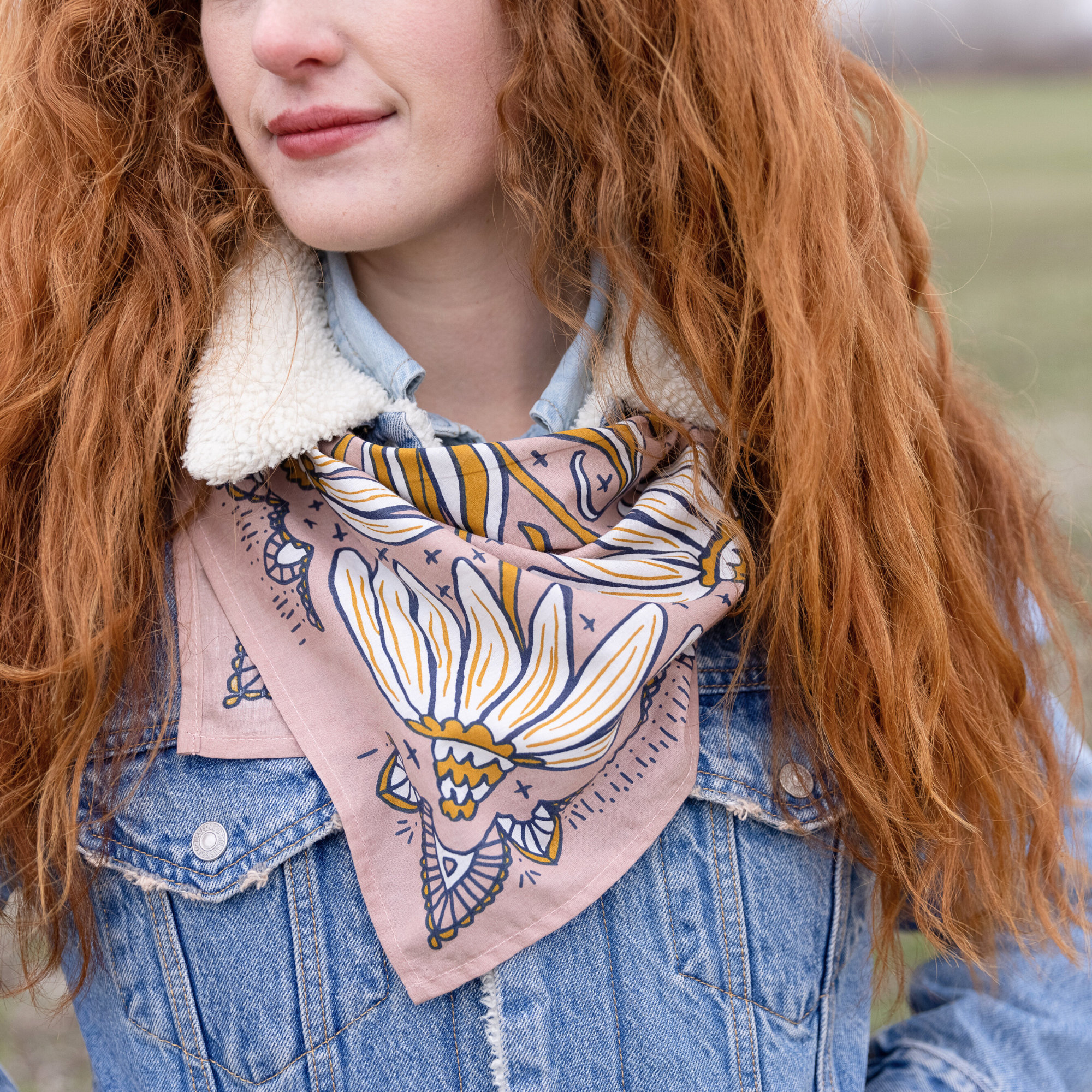 Person with red hair wearing a denim jacket and patterned scarf