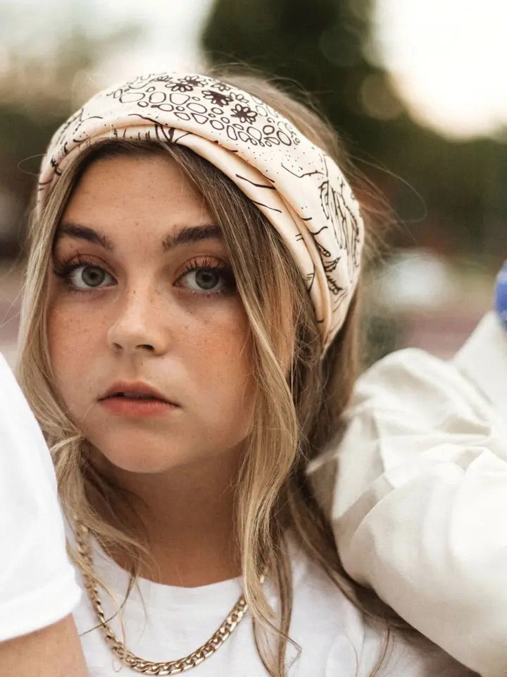 Front close-up of Desert bandana worn as a wide headband, cream with brown screen printed desert and floral pattern
