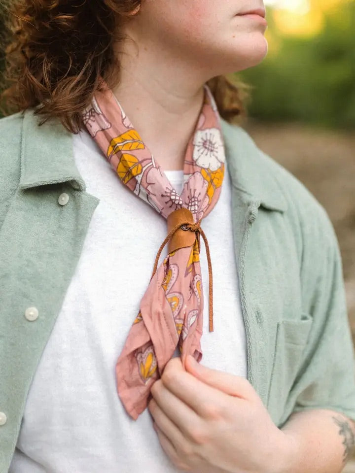 Neck close-up of Evangeline bandana showing pink floral and mustard print with leather slide, worn over white tee and sage jacket