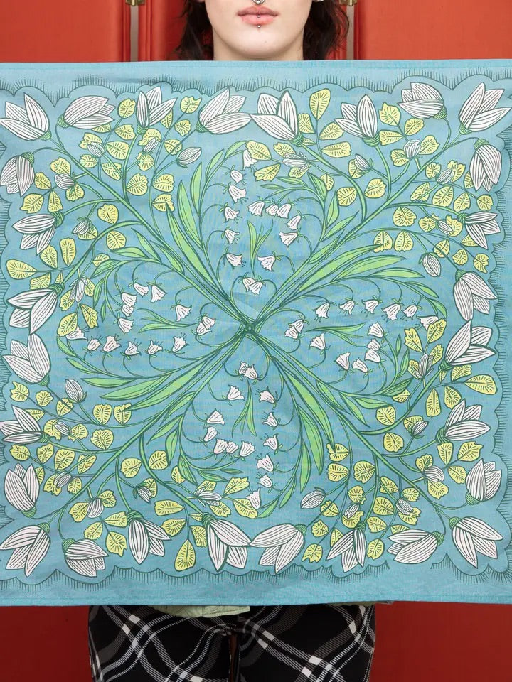 Front view of Cassie bandana showing teal floral background with hand-drawn white bell-shaped flowers, green leaves, and scalloped border held in front of a red door
