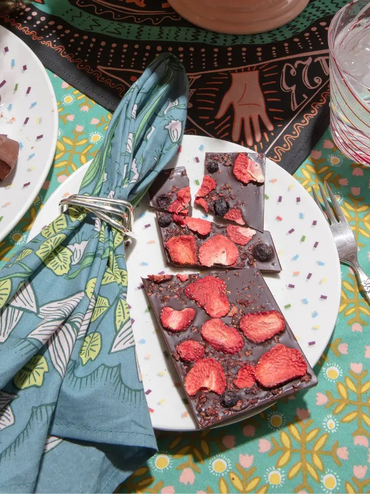 Flat lay of No. 096 Cassie bandana folded in a napkin ring showing teal floral print on cotton against a colorful table